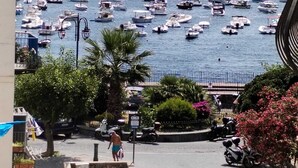 A marina with numerous boats docked, a clear sky, and a street with parked scooters and a pedestrian. - Ischia Ponte Romantic Apartment in the Historical Center and Near the sea (Ischia)