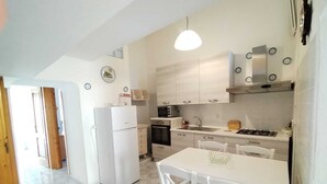 A modern kitchen with white cabinets, a refrigerator, a microwave, and a dining area with a table and chairs. - Ischia Ponte Romantic Apartment in the Historical Center and Near the sea (Ischia)