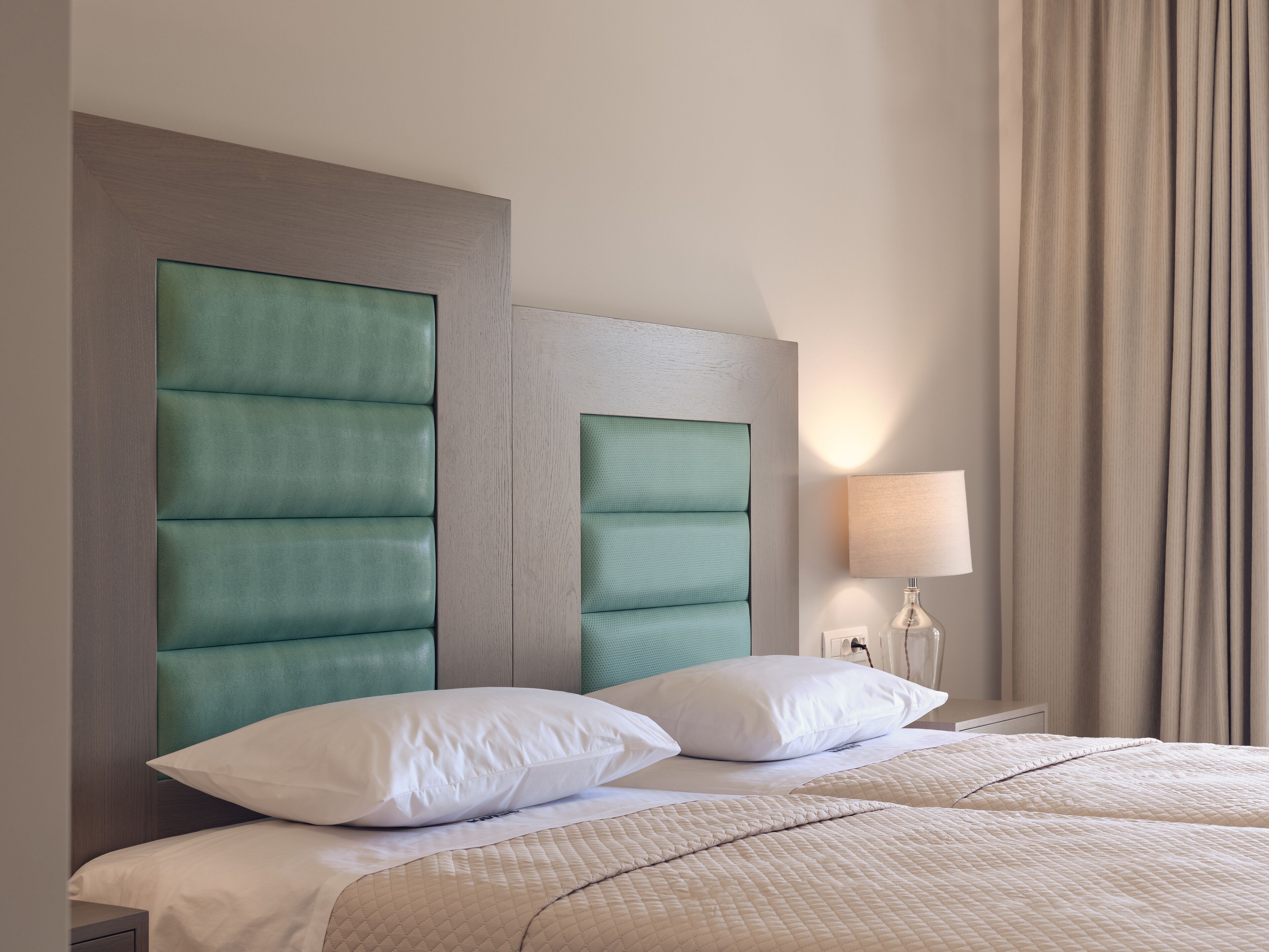 Une chambre d’hôtel avec un grand lit, deux oreillers, une table de chevet avec une lampe et une fenêtre avec des rideaux.