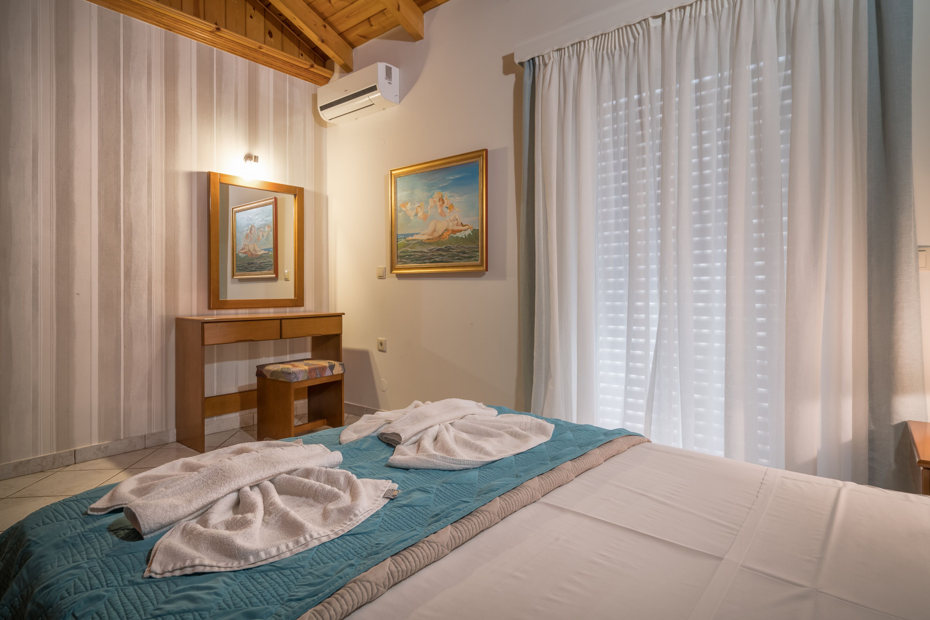A hotel room with a bed, two towels, a desk, a chair, and two paintings on the wall.