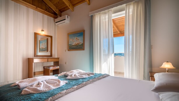 Une chambre d’hôtel avec un lit, une table de chevet, une lampe, un tableau et une vue sur la mer.