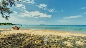 Une plage à l’eau claire, un bateau à l’horizon et une personne se détendant sur le sable.