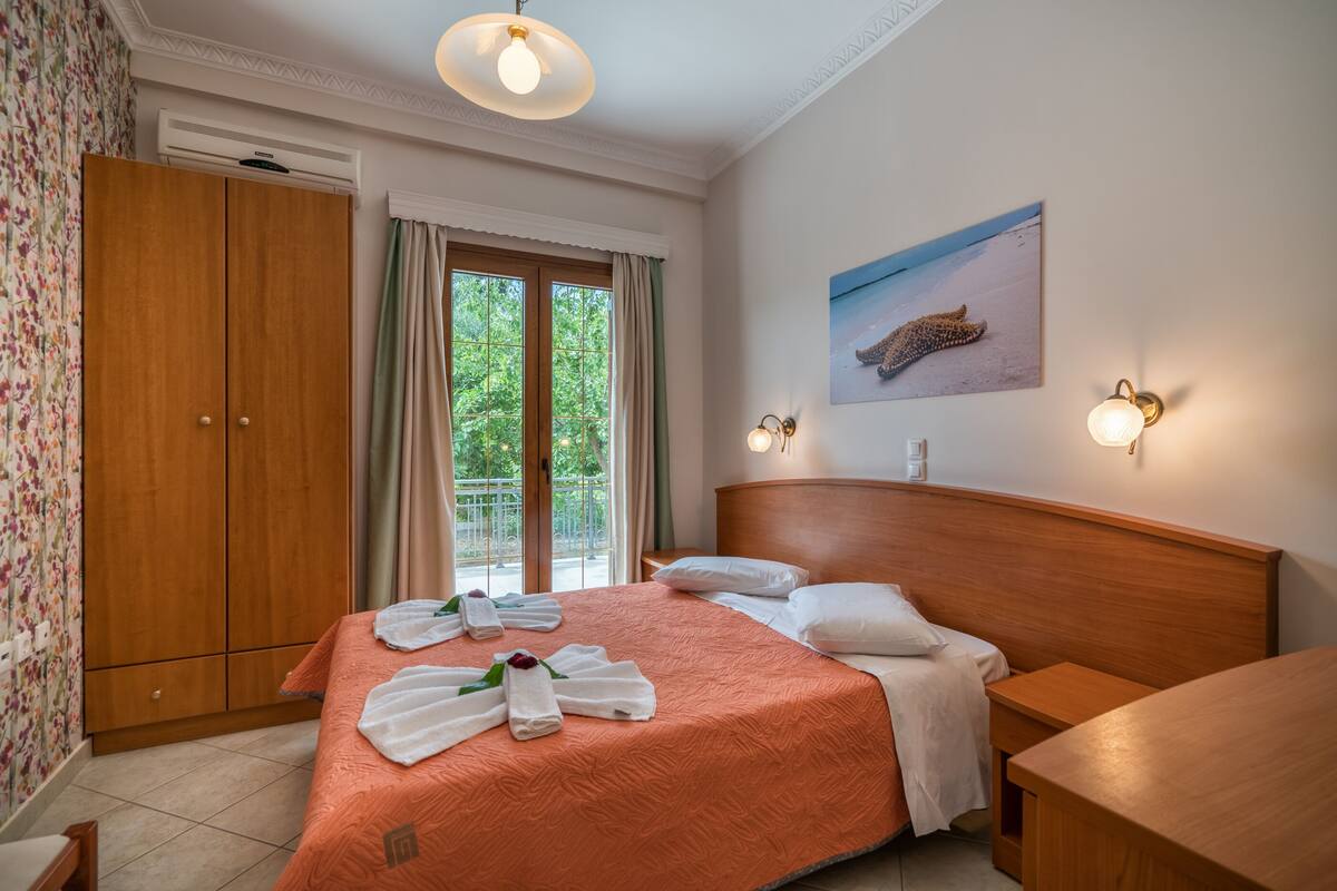 A bedroom with a wooden bed, a wooden wardrobe, a bedside table, and a window with curtains.