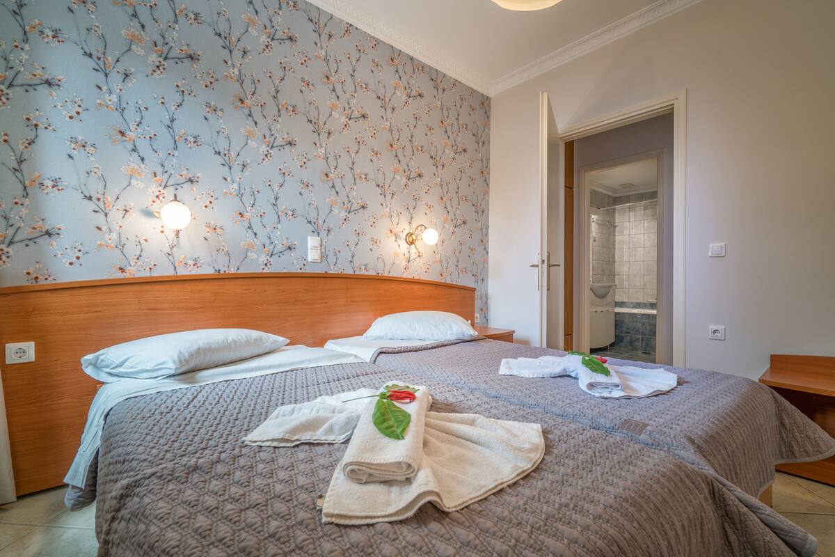 A neatly made bed with a floral wallpaper, two bedside lamps, and a visible bathroom door.