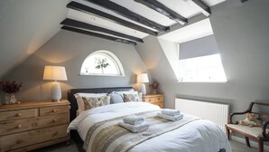 Un dormitorio con una cama grande, dos mesitas de noche, un aparador, un ventanal con vistas y un banco de madera.
