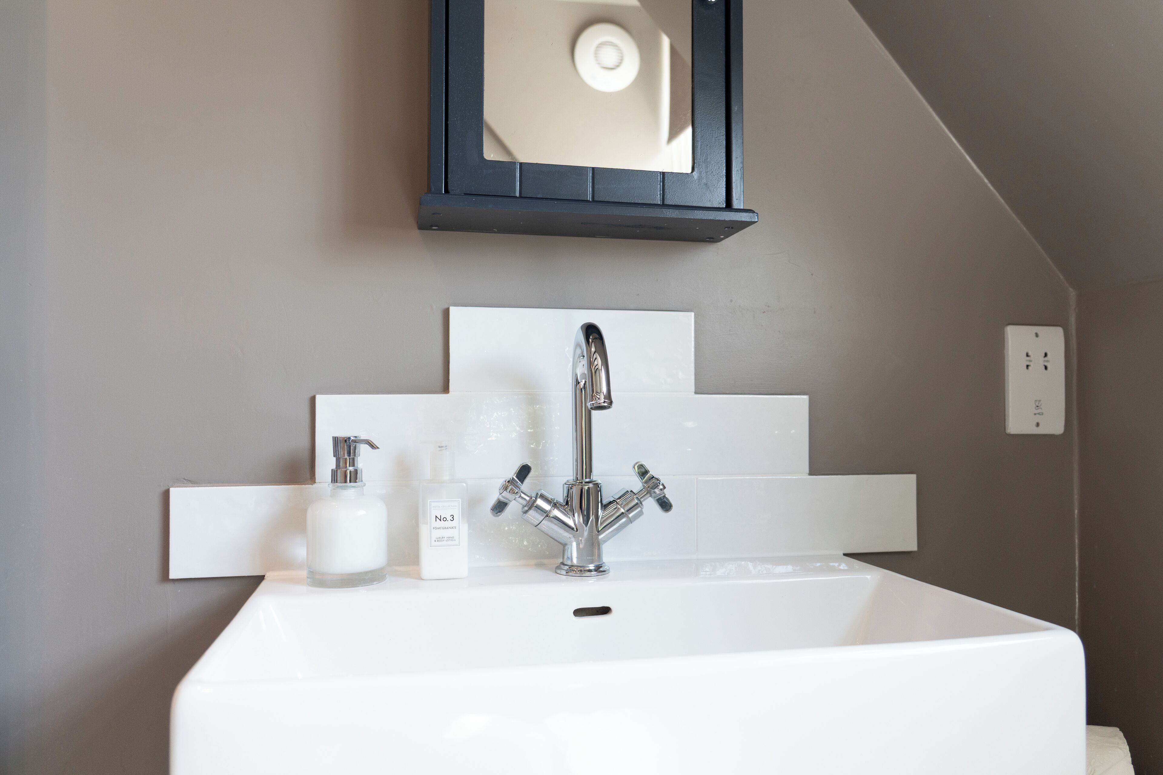 A bathroom with a white sink, a mirror, and a pomegranate hand and body lotion dispenser.