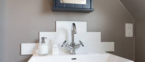 A bathroom with a white sink, a mirror, and a pomegranate hand and body lotion dispenser.