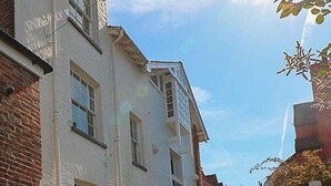 Una estrecha calle adoquinada flanqueada por edificios blancos, algunos con fachadas de ladrillo, y un cielo azul despejado.