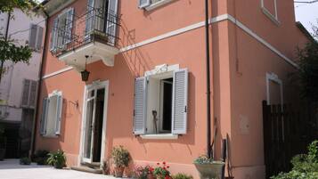 A two-story building with a balcony, potted plants, and a door with a window.