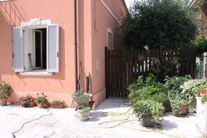 A courtyard with potted plants, a wooden fence, and a building with a window and shutters. - Villa Al Mare Rimini (Rimini)
