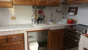 A kitchen with wooden cabinets, a white tiled backsplash, a sink, a stove, and a trash bin. - Villa Al Mare Rimini (Rimini)