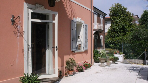 A building with a white door and shutters, potted plants, and a tiled patio. - Villa Al Mare Rimini (Rimini)