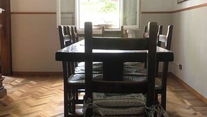 A dining area with a wooden table and chairs, a chandelier, and a large window with curtains. - Villa Al Mare Rimini (Rimini)