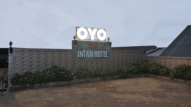 A sign for the Oyo Intan Motel with a rustic brick wall and a clear sky.