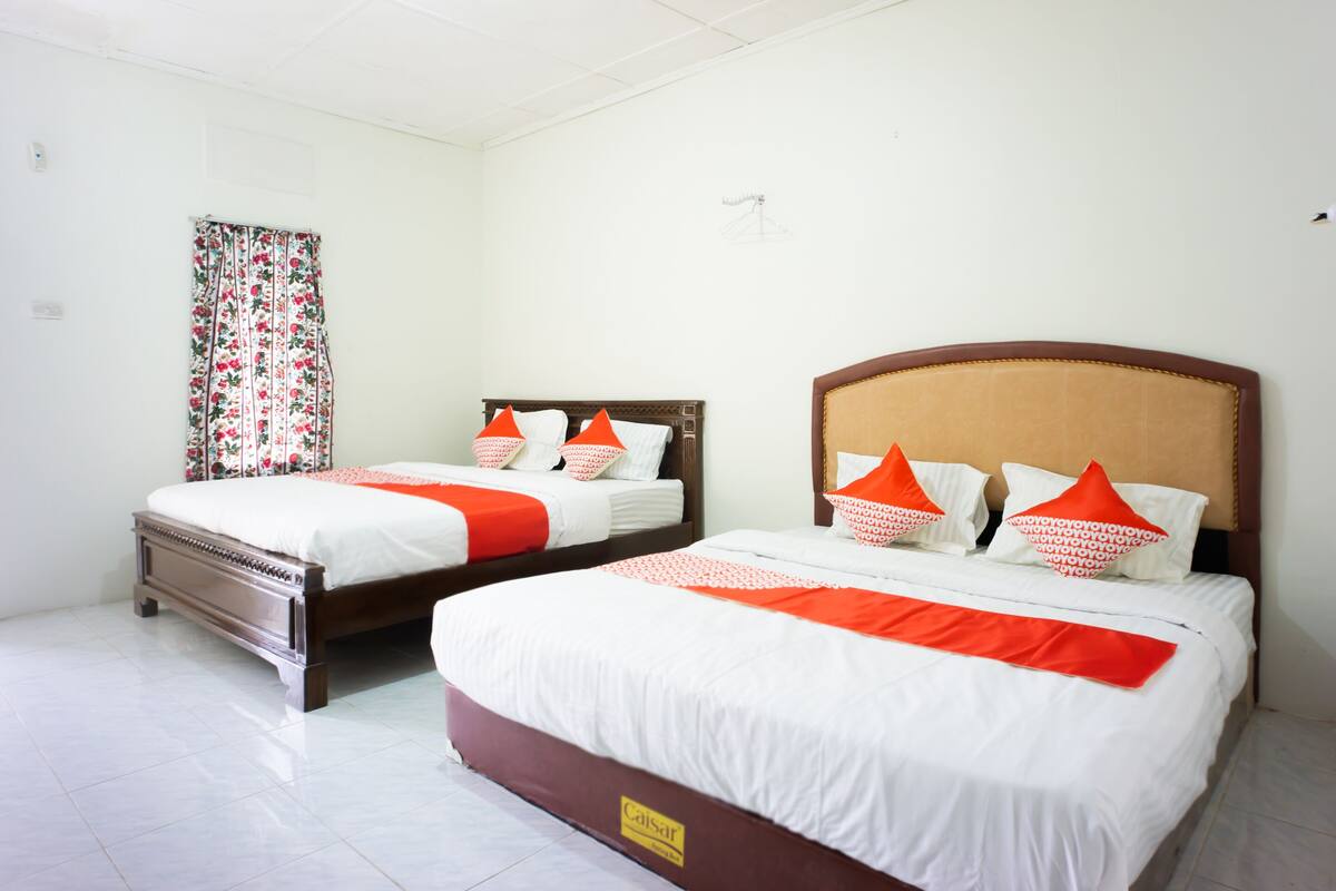 Two beds with white and orange bedding, a floral curtain, and a wooden headboard.