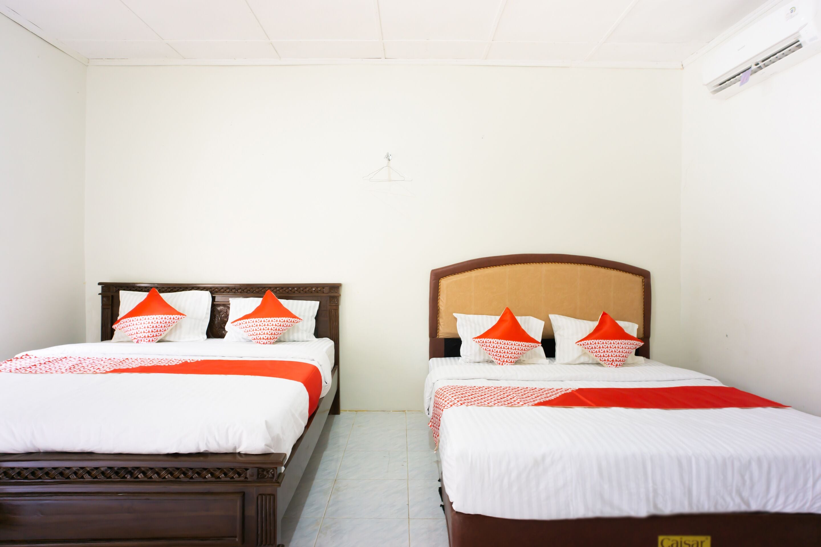 A hotel room with two beds, each with white bedding and orange pillows, and a wooden headboard.