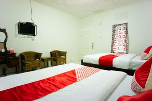 A hotel room with two beds, a television, a wooden chair, a desk, and a window with floral curtains.