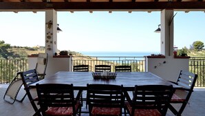 A covered patio with a table and chairs, overlooking a coastal landscape.