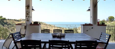 A covered patio with a table and chairs, overlooking a coastal landscape.