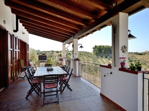 Un patio cubierto con una mesa, sillas, un televisor y vistas al campo.