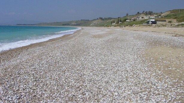 A pebbled beach with a clear view of the ocean and distant buildings.