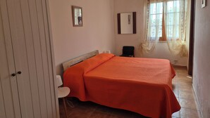 A bedroom with a bed, a chair, a wardrobe, and a window with curtains.