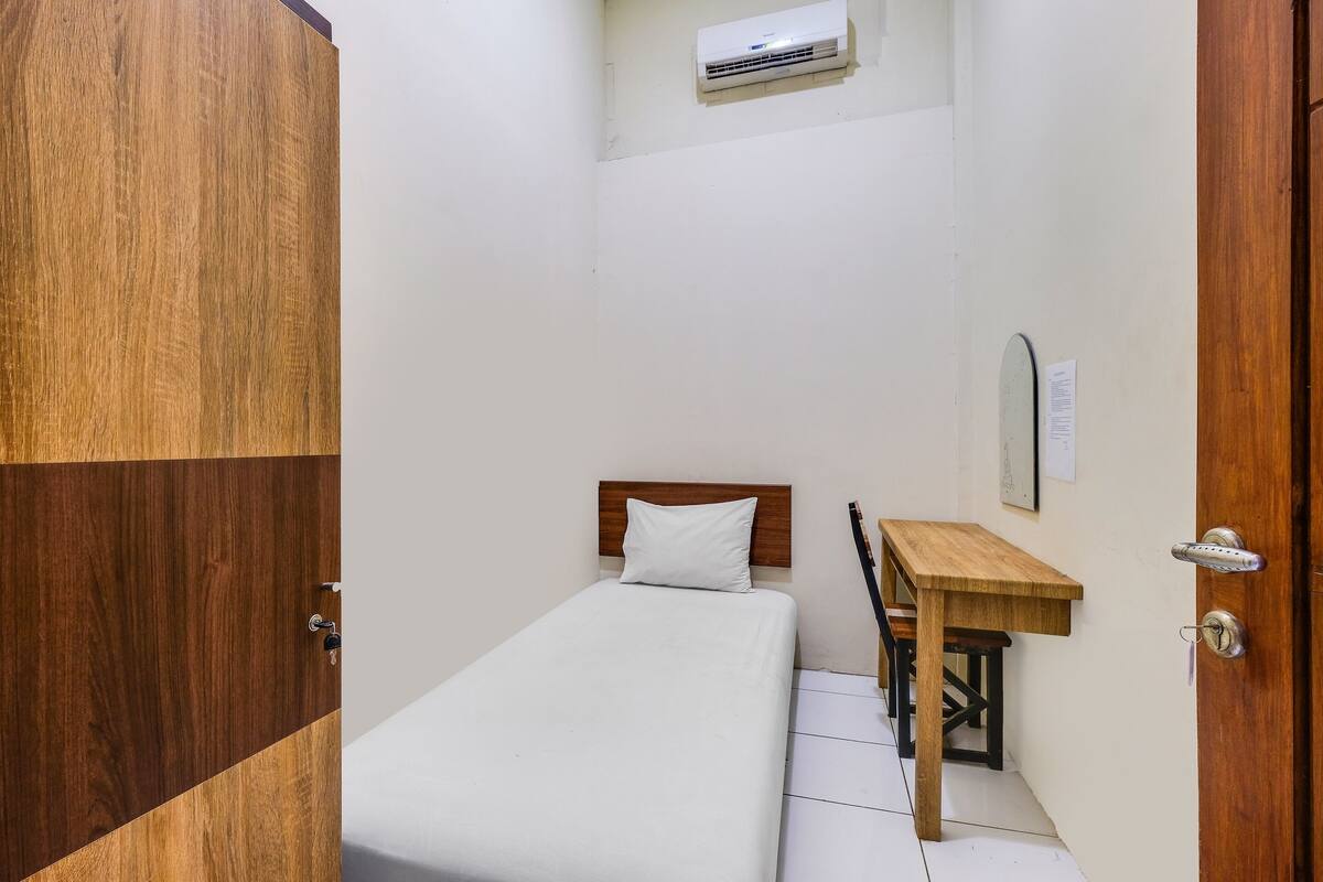 Un dormitorio pequeño y ordenado con una cama, un escritorio de madera y un equipo de aire acondicionado en la pared.