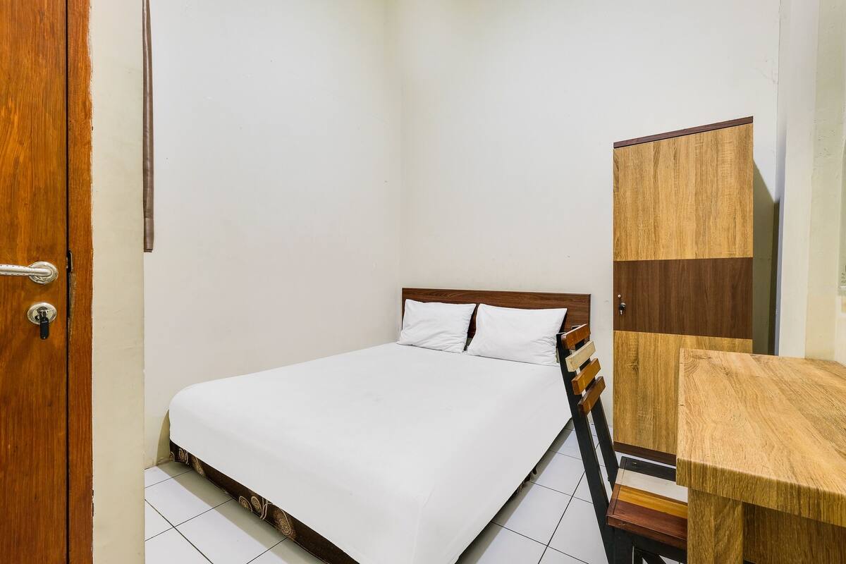 Un dormitorio pequeño y ordenado con cama, un escritorio de madera y un armario.
