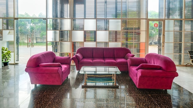 A spacious lobby with a modern design, featuring a large seating area with a purple sofa set and matching armchairs, a glass coffee table, and a view through large windows with blinds. - Hotel O Camel Residence (Semarang)