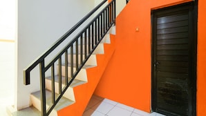 A staircase with black railings leading to a room with an orange wall and a black door. - Hotel O Camel Residence (Semarang)