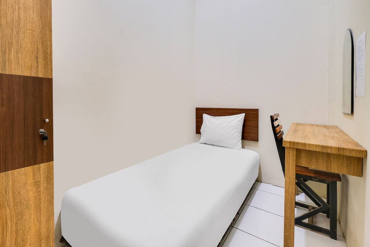 Una habitación pequeña y ordenada con una cama individual, un escritorio de madera y una puerta.