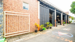 A street view with a brick building, a metal gate, and potted plants. - Hotel O Camel Residence (Semarang)