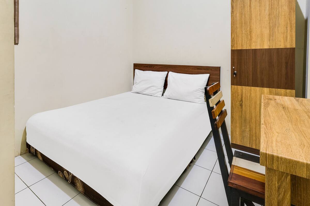 Habitación con una cama individual, cabecera de madera, ropa de cama blanca y un armario de madera.