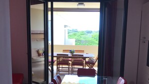 Ein Essbereich mit einem Glastisch und roten Stühlen, einer roten Pendelleuchte sowie Blick auf einen Balkon mit Tisch und Stühlen.