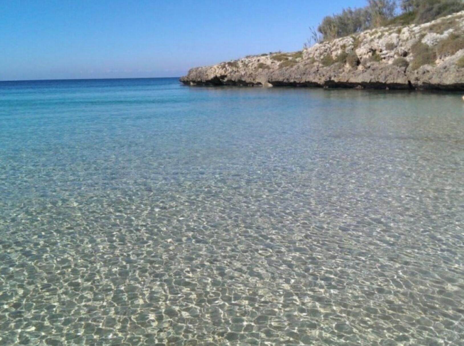 A clear coastal beach with rocky terrain and calm waters.