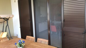 Ein Holztisch mit Stühlen, eine Blumenvase und eine Glastür mit Jalousien.