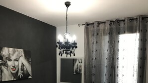 Ein Schlafzimmer mit Bett, Nachttisch, Lampe, einer Deckenleuchte und einem Fenster mit Vorhängen.