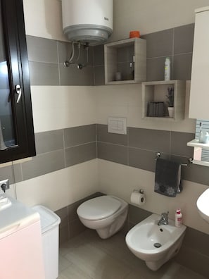 Ein Badezimmer mit Toilette, Bidet und Waschbecken, mit gefliesten Wänden und einem Handtuchhalter.