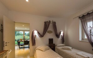 A bedroom with two beds, a window with curtains, a bedside table, and a view of a dining area. - Hillside Villa With Swimming Pool and Jacuzzi of the Marche (Sassoferrato)
