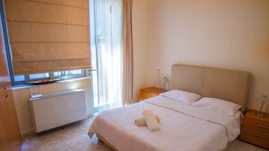 A hotel room with a bed, a bedside table, a lamp, a window with a blind, and a radiator. - Luxurious Villa Ariadni Theseus Crete (Malevizi)