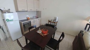 A compact kitchen with a refrigerator, oven, and sink. There is a dining table with chairs and a small side table with a lamp. - Luxurious Villa Ariadni Theseus Crete (Malevizi)
