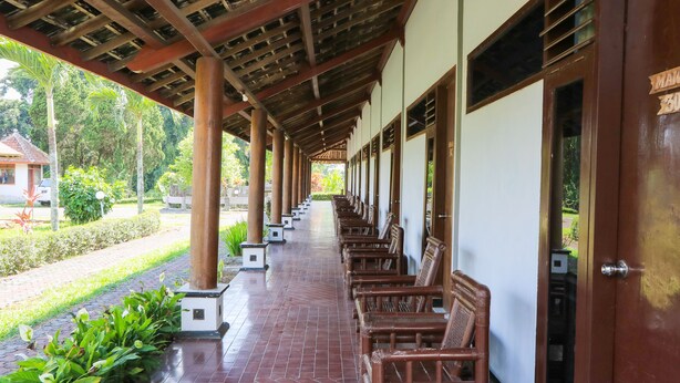 A covered walkway with wooden benches, columns, and a tiled floor.