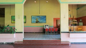 A building entrance with a large archway, a framed poster on the wall, and a few red chairs outside.
