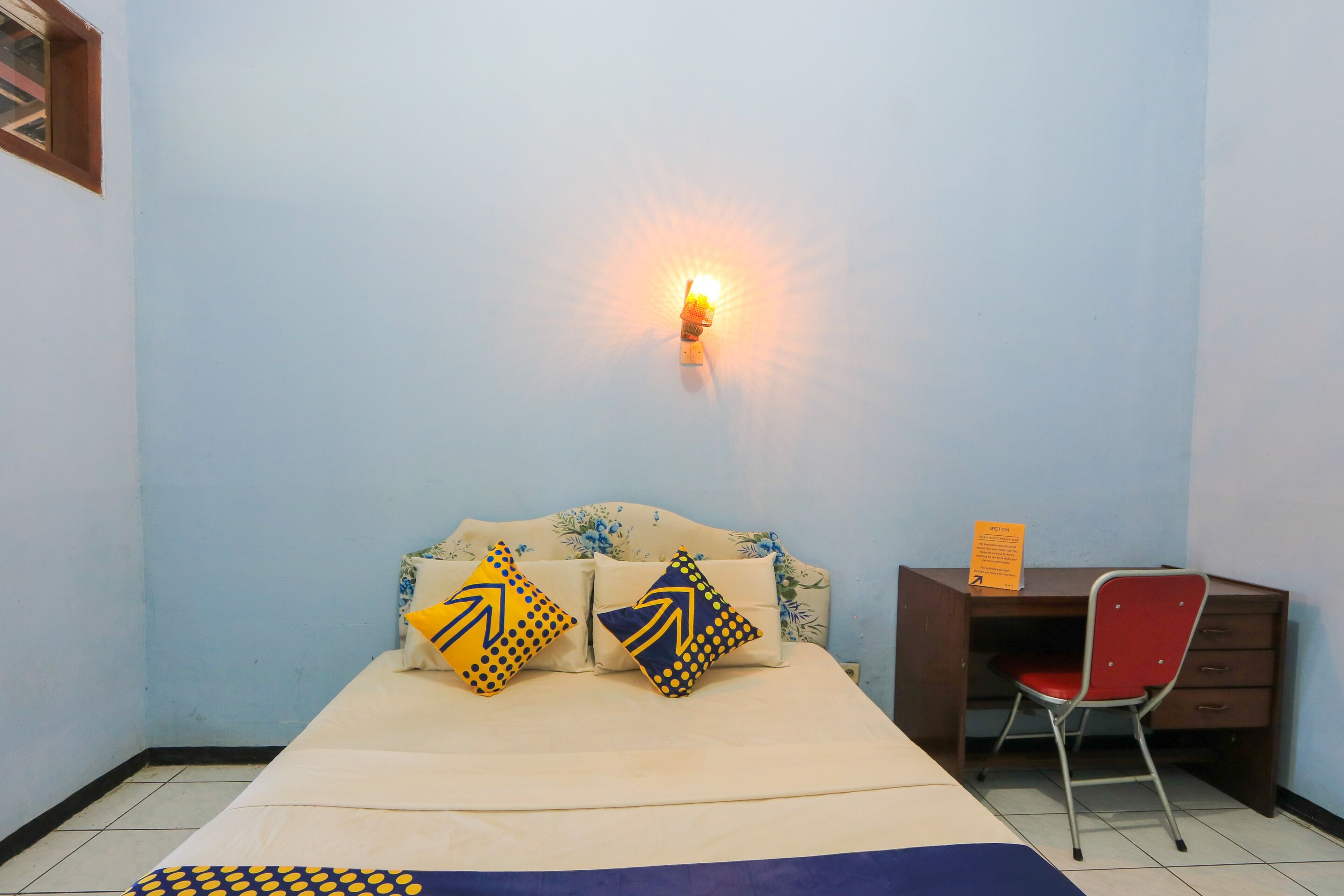 Une pièce comprenant un lit, un bureau et une chaise. Un luminaire est fixé au mur au-dessus du lit.