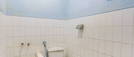 Een kleine betegelde badkamer met een toilet, een handdroger en een blauwe leiding.