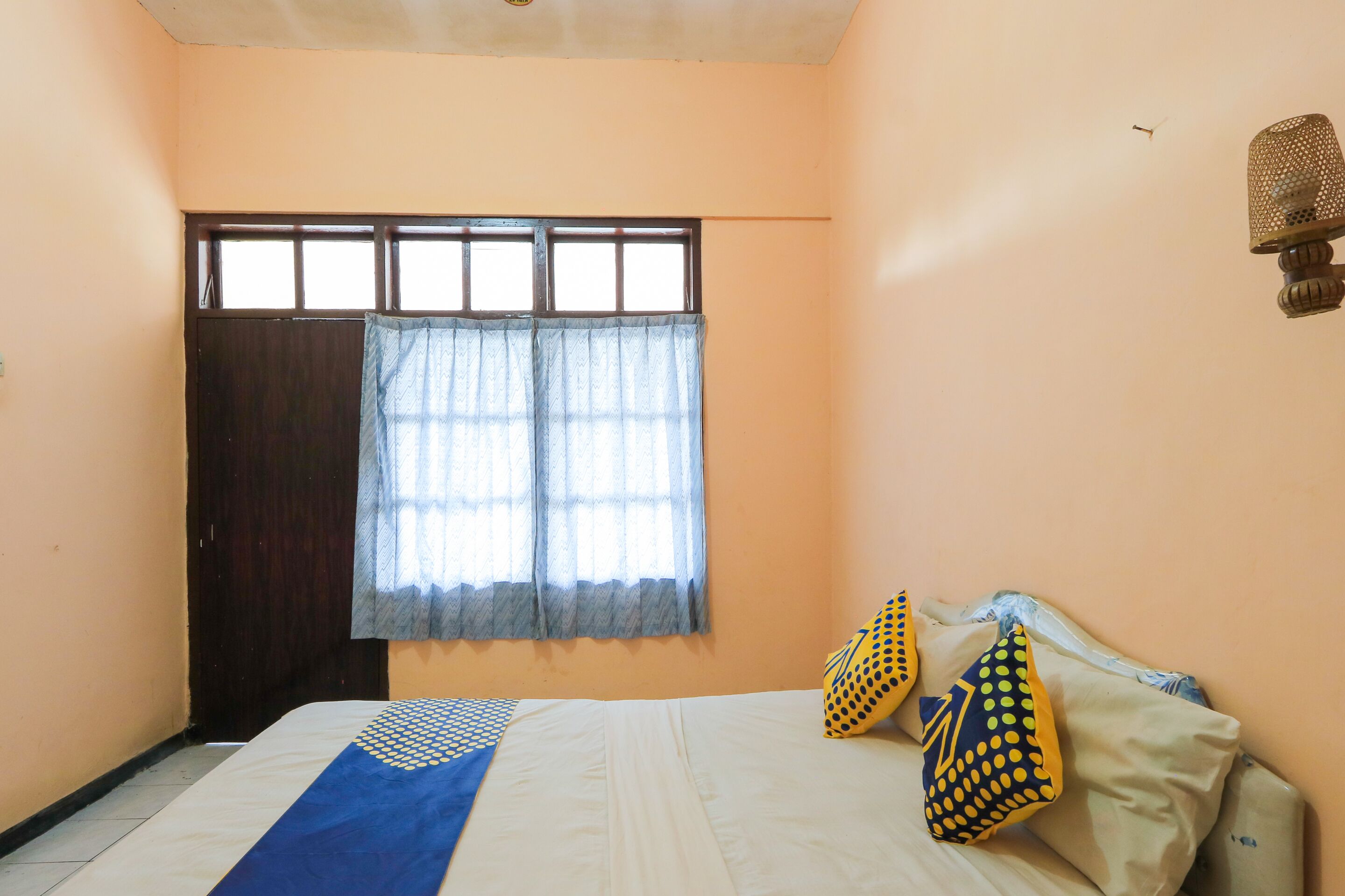 A room with a bed, a window with curtains, and a wall-mounted lamp.