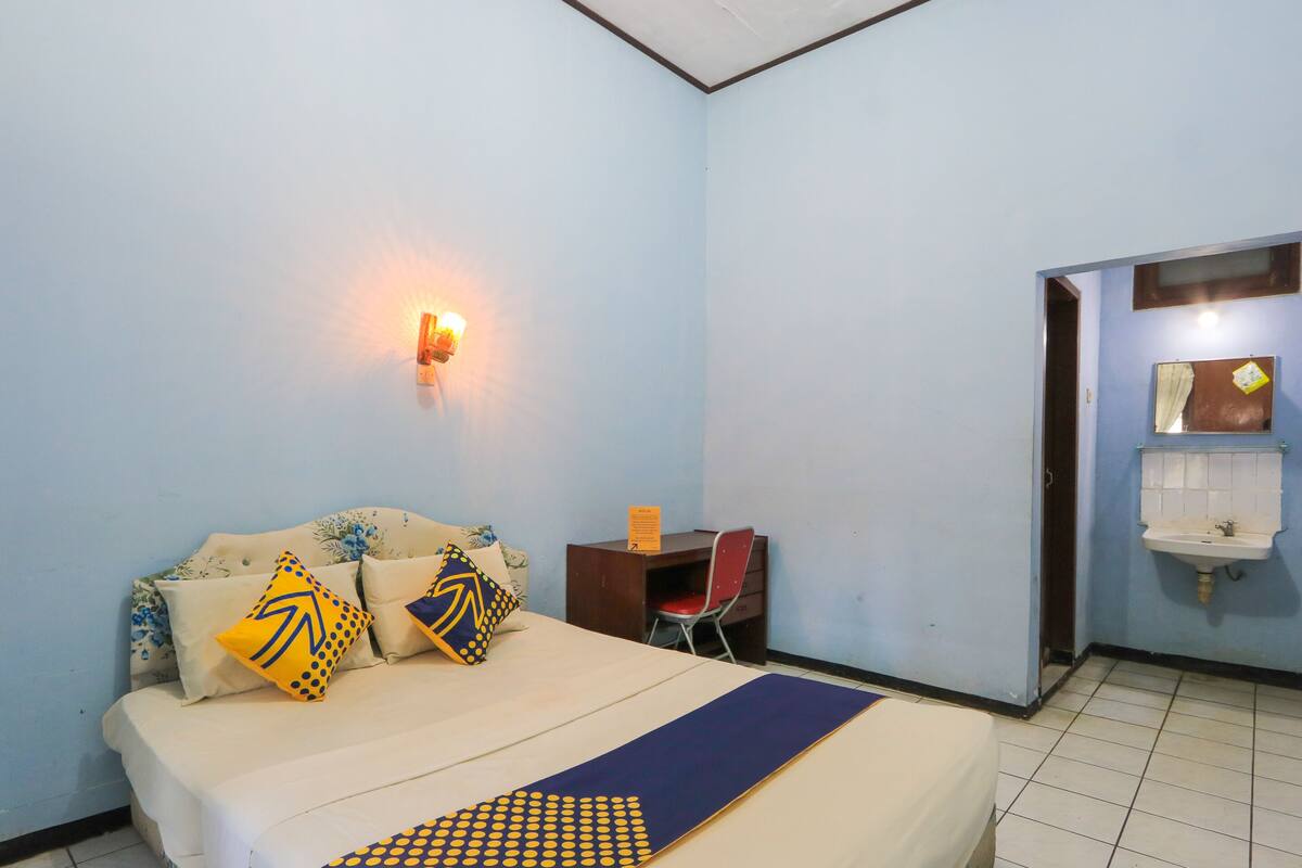Une chambre à coucher avec un lit, des oreillers, un bureau et un lavabo fixé au mur.