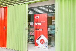 A hotel entrance with a green and red facade, a prominent OYO Hotels promotional banner, and a visible entrance door. - OYO 2354 3 Point Residence (Surabaya)