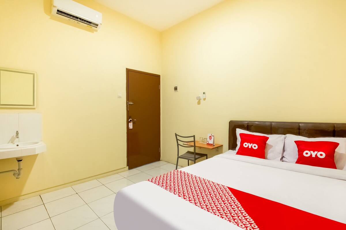 A hotel room with a bed, a bedside table, a chair, a sink, and a door.