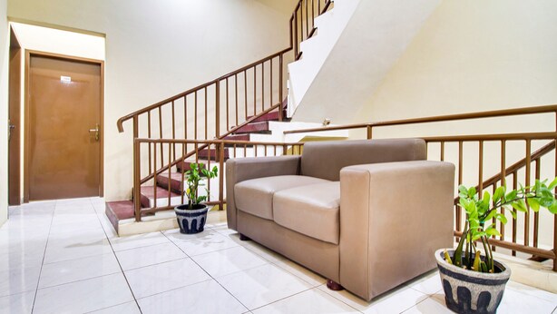 A living room with a beige sofa, two potted plants, a staircase, and a wooden door. - OYO 2354 3 Point Residence (Surabaya)